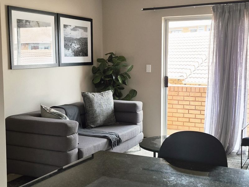 An open-plan living area featuring a modern kitchen with granite countertops and cabinetry, flowing into a lounge space with access to a balcony.