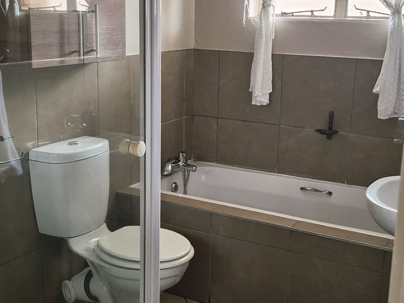 A functional bathroom featuring a shower enclosure, bathtub, toilet, and wall-mounted vanity cabinet with neutral tiled finishes.