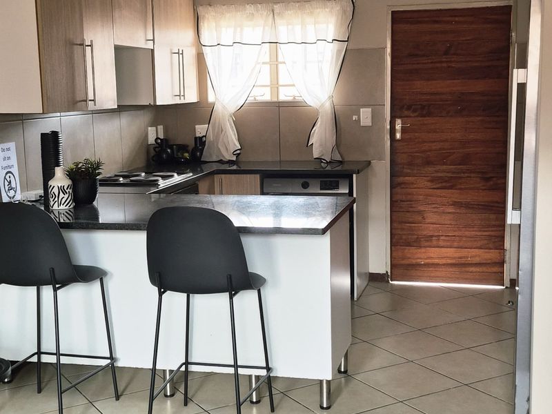 A functional kitchen featuring light wood cabinetry, granite countertops, a breakfast bar, and tiled flooring, with direct access to an exterior timber door.