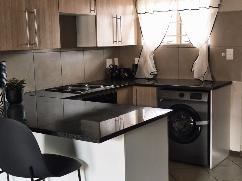 Compact kitchen featuring light wood cabinetry, dark granite countertops, tiled flooring, and a built-in electric hob with an integrated washing machine.