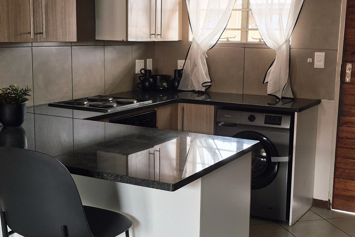 A functional kitchen featuring wood-finish cabinetry, dark granite countertops, a built-in hob, and tiled flooring with an integrated washing machine.