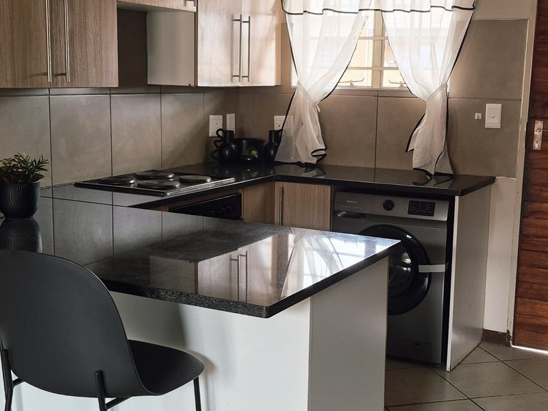 A functional kitchen featuring wood-finish cabinetry, dark granite countertops, a built-in hob, and tiled flooring with an integrated washing machine.