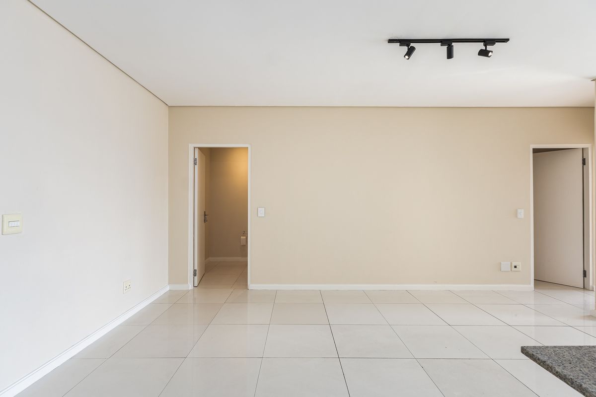 A bright, empty living area featuring neutral walls, large format floor tiles, and modern track lighting, providing a clean canvas for interior design.