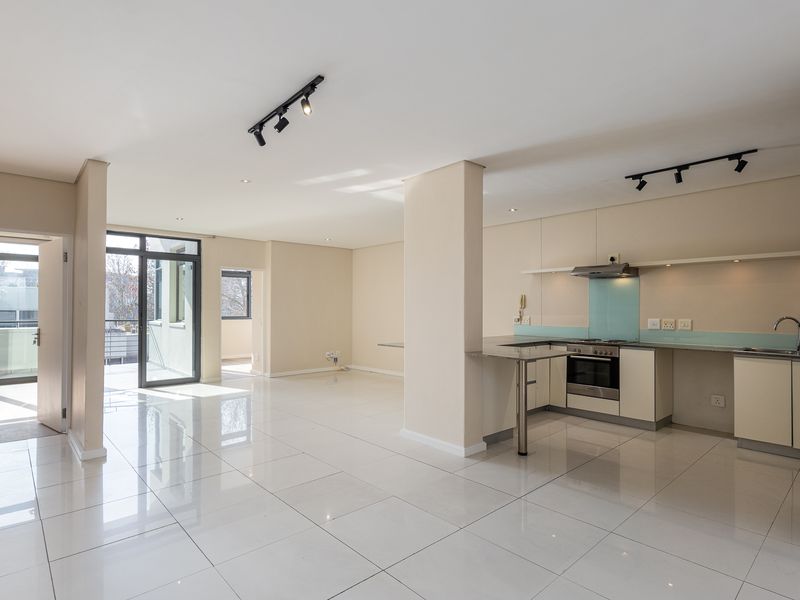Spacious open-plan living area featuring a modern kitchen with built-in appliances, sleek tiled flooring, and direct access to a balcony through sliding glass doors.