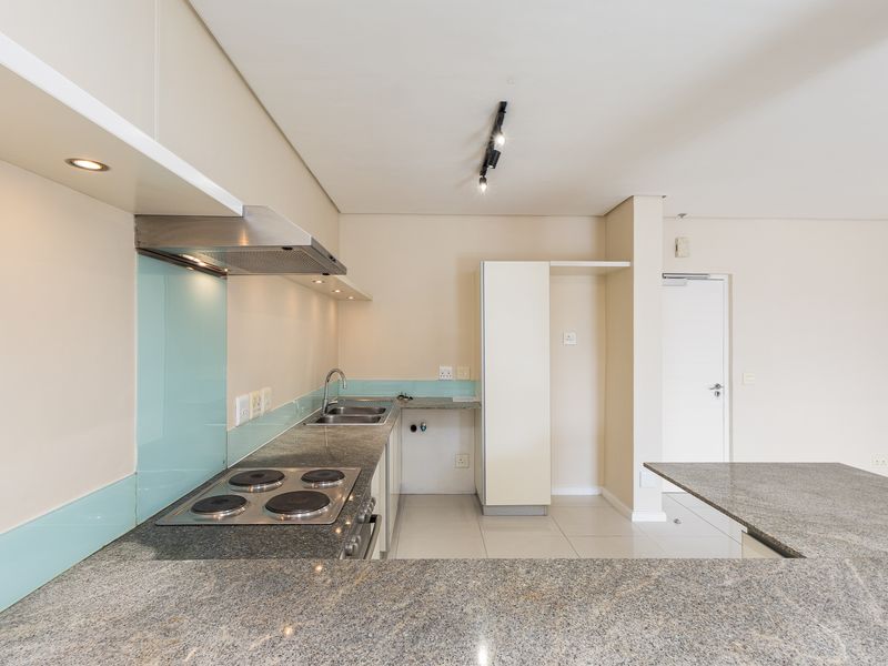 Modern kitchen featuring granite countertops, an electric hob with extractor fan, glass splashback, and ample built-in cabinetry in an open-plan layout.