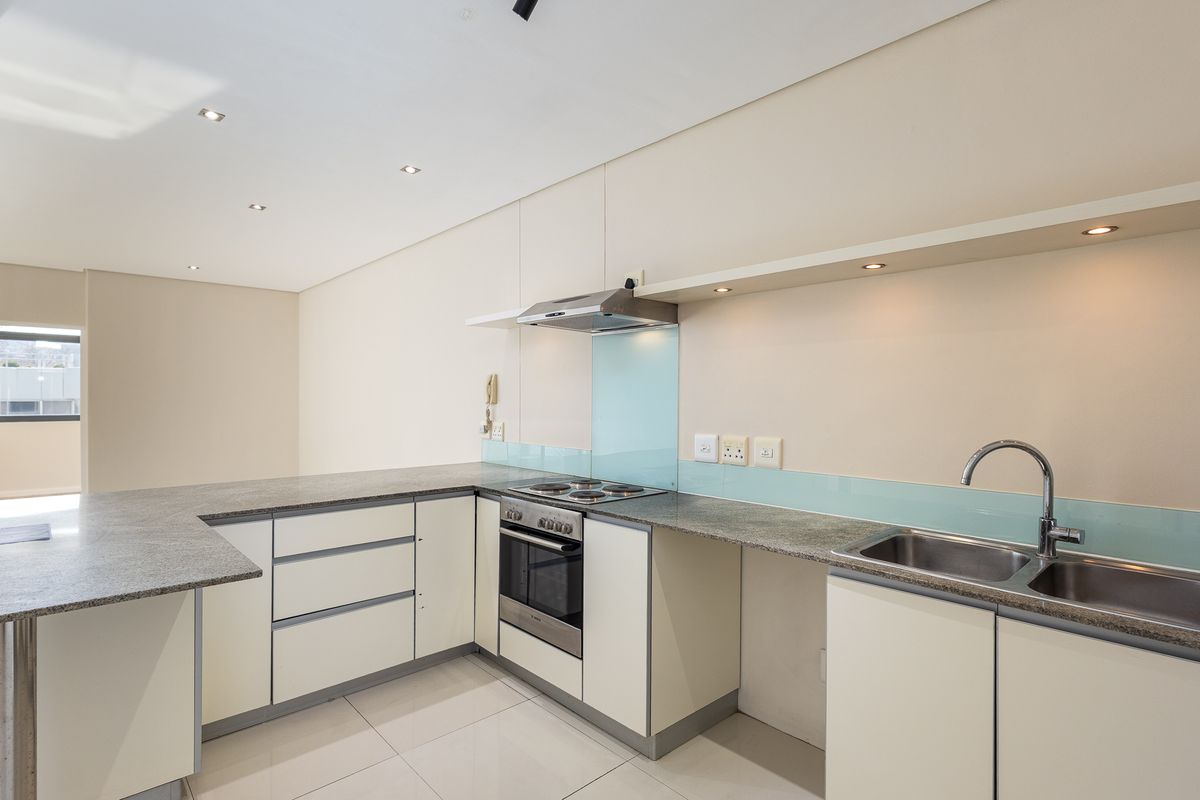 Modern kitchen featuring granite countertops, built-in oven, electric hob, extractor fan, and a stainless steel double sink with glass splashback.