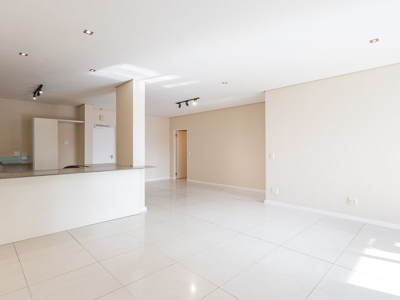 Spacious open-plan living and kitchen area featuring neutral tones, polished tile flooring, recessed lighting, and a functional kitchen with granite countertops.