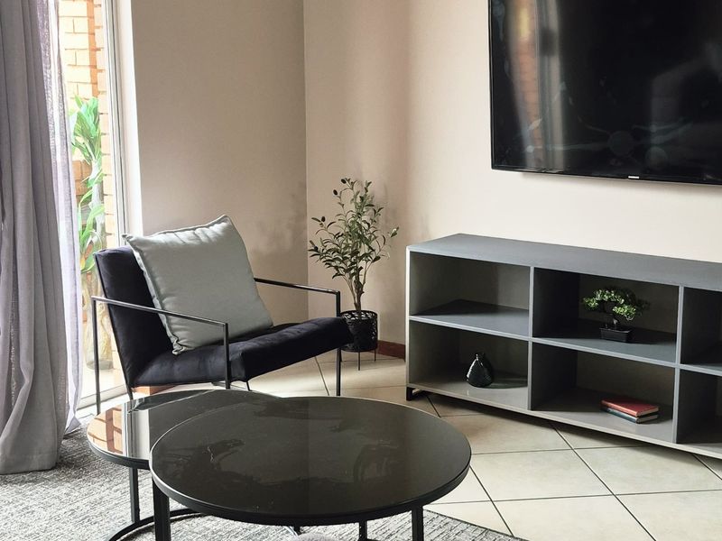 A well-maintained living room featuring neutral wall tones, tiled flooring, and a sliding glass door providing natural light and access to the exterior.