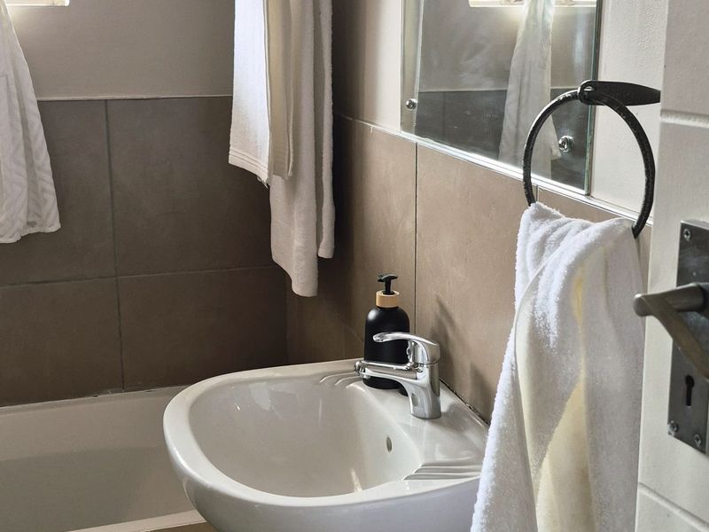 A functional bathroom featuring a pedestal basin, mixer tap, bathtub, and neutral wall tiling with integrated towel fixtures and a wall-mounted mirror.