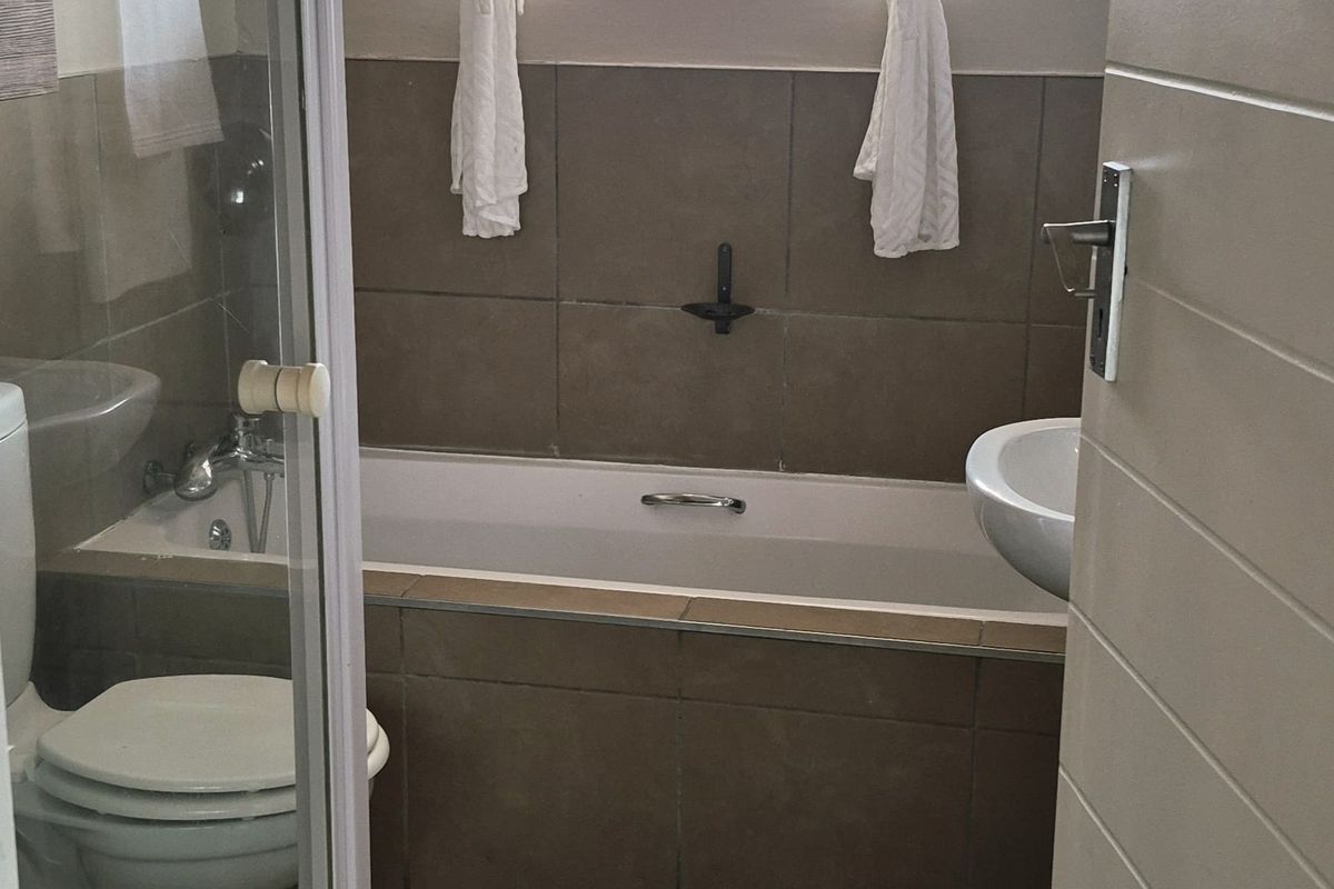 A functional bathroom featuring a bathtub, separate shower enclosure, pedestal basin, and tiled finishes throughout.