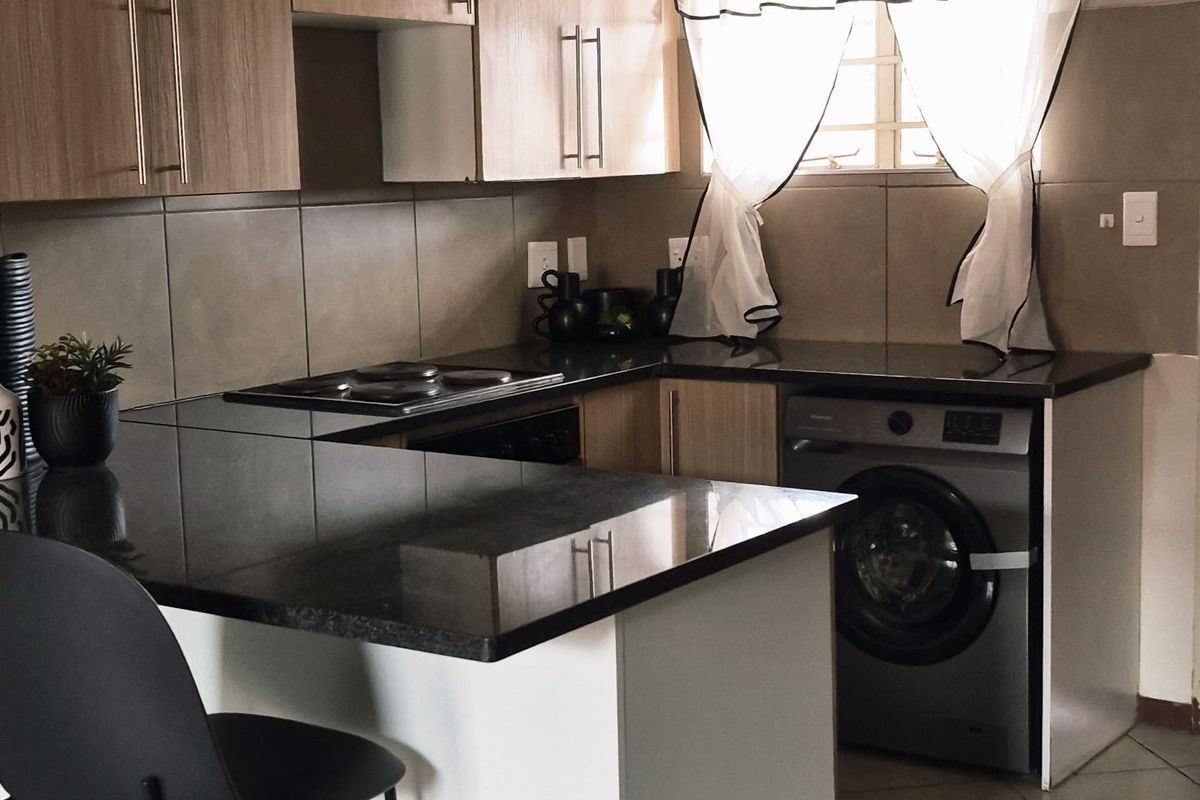 Compact kitchen featuring light wood cabinetry, dark granite countertops, tiled flooring, and a built-in electric hob with an integrated washing machine.