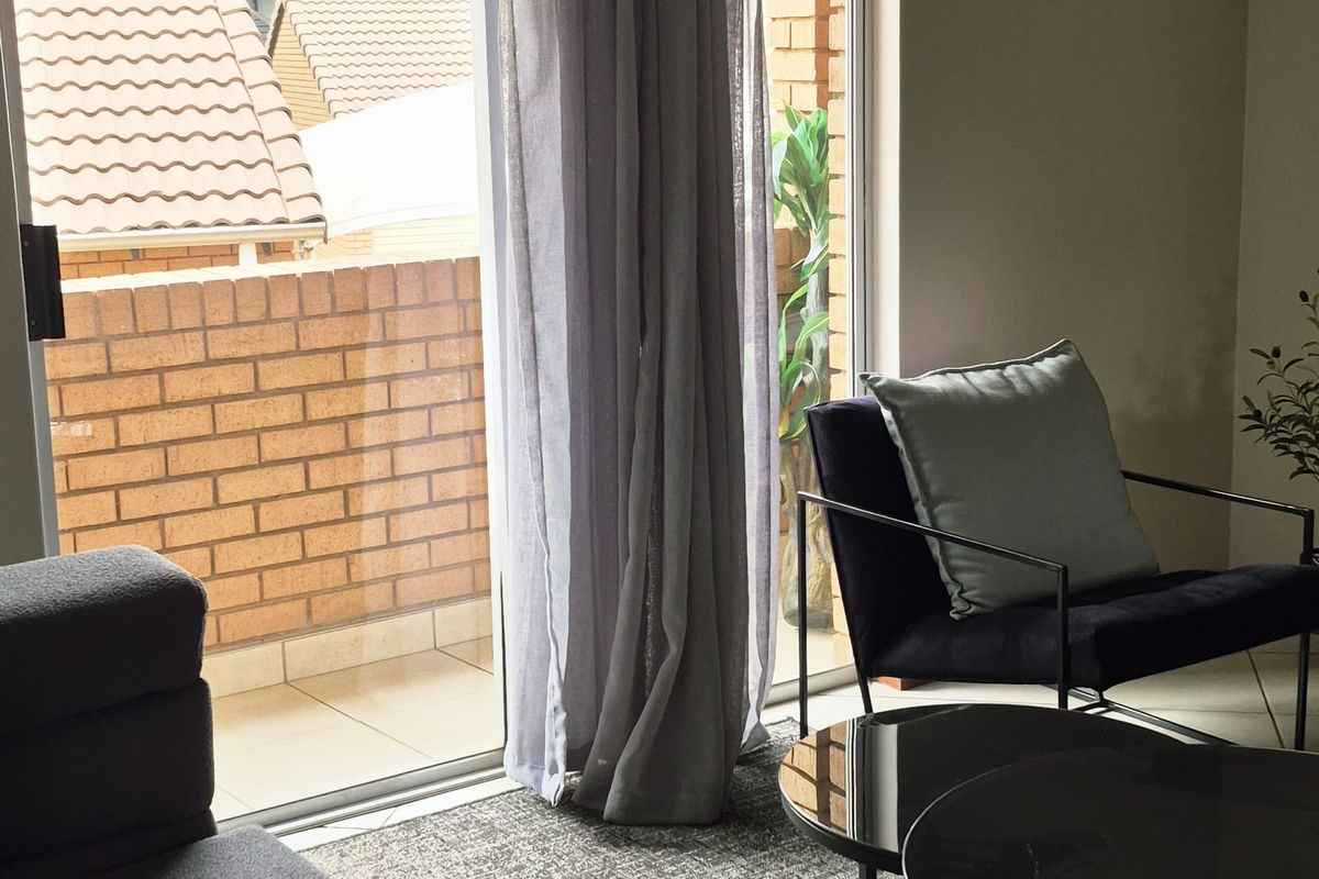 A comfortable living room featuring a large sliding glass door that opens onto a private balcony with brick detailing.