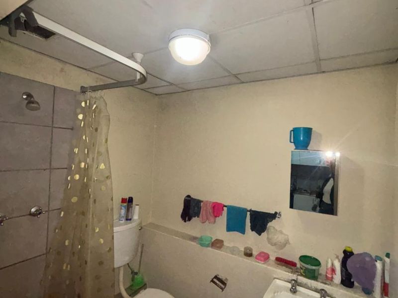 A compact bathroom featuring a pedestal sink, toilet, and shower area with a drop ceiling, currently requiring cosmetic updates and maintenance.