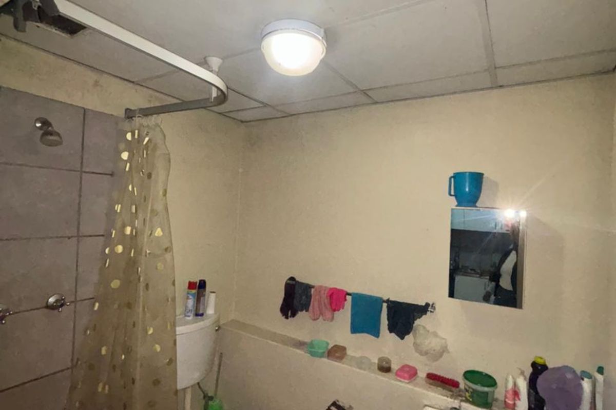 A compact bathroom featuring a pedestal sink, toilet, and shower area with a drop ceiling, currently requiring cosmetic updates and maintenance.