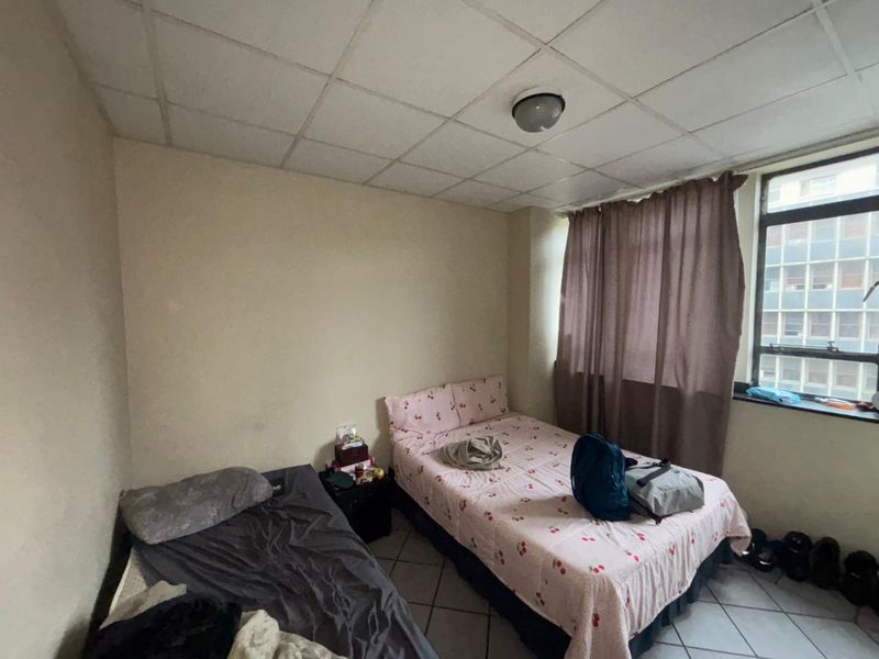 A bedroom featuring tiled flooring, a drop ceiling, and a large window, currently requiring cosmetic updates to improve its overall condition.