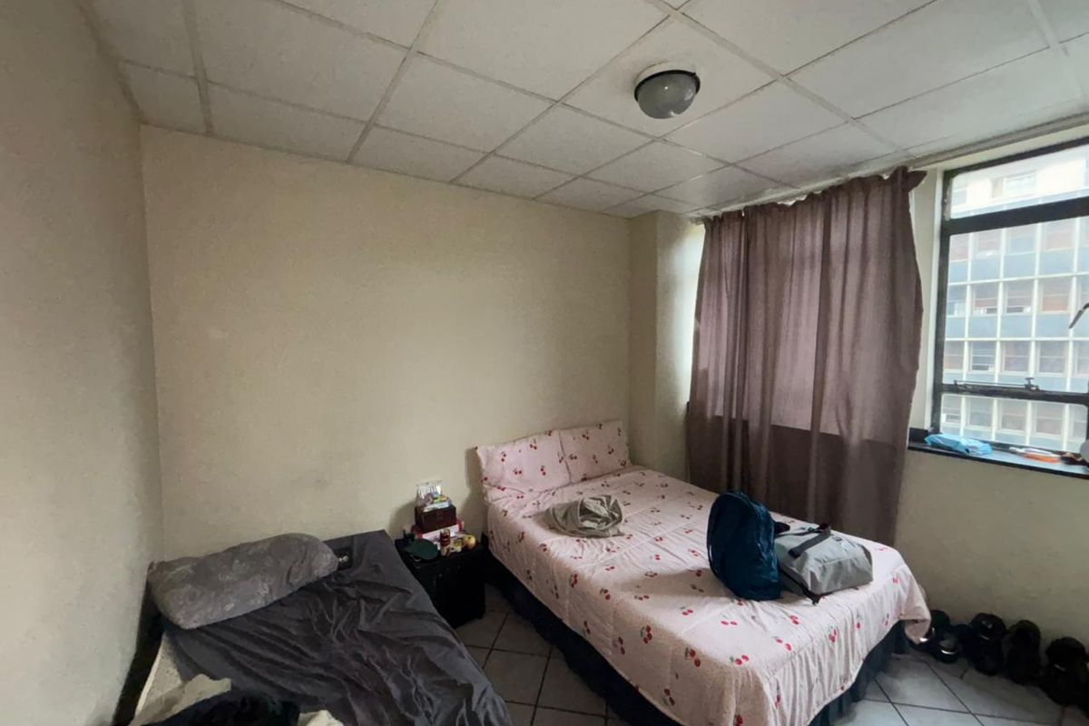 A bedroom featuring tiled flooring, a drop ceiling, and a large window, currently requiring cosmetic updates to improve its overall condition.
