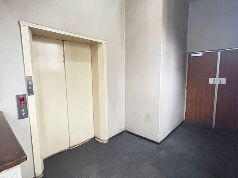 A functional apartment building hallway featuring an elevator and double access doors, showing signs of wear and requiring cosmetic updates.
