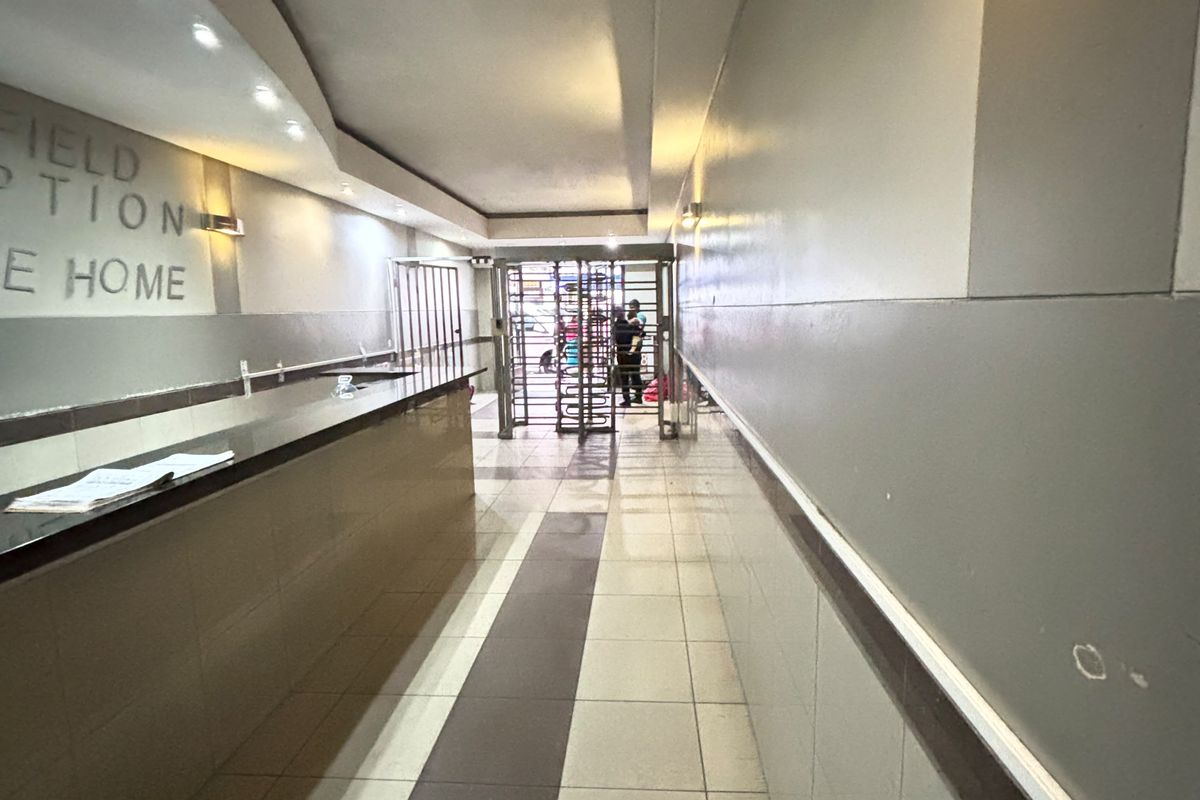 A functional apartment building entrance lobby featuring a reception desk, tiled flooring, and a secure turnstile access point.