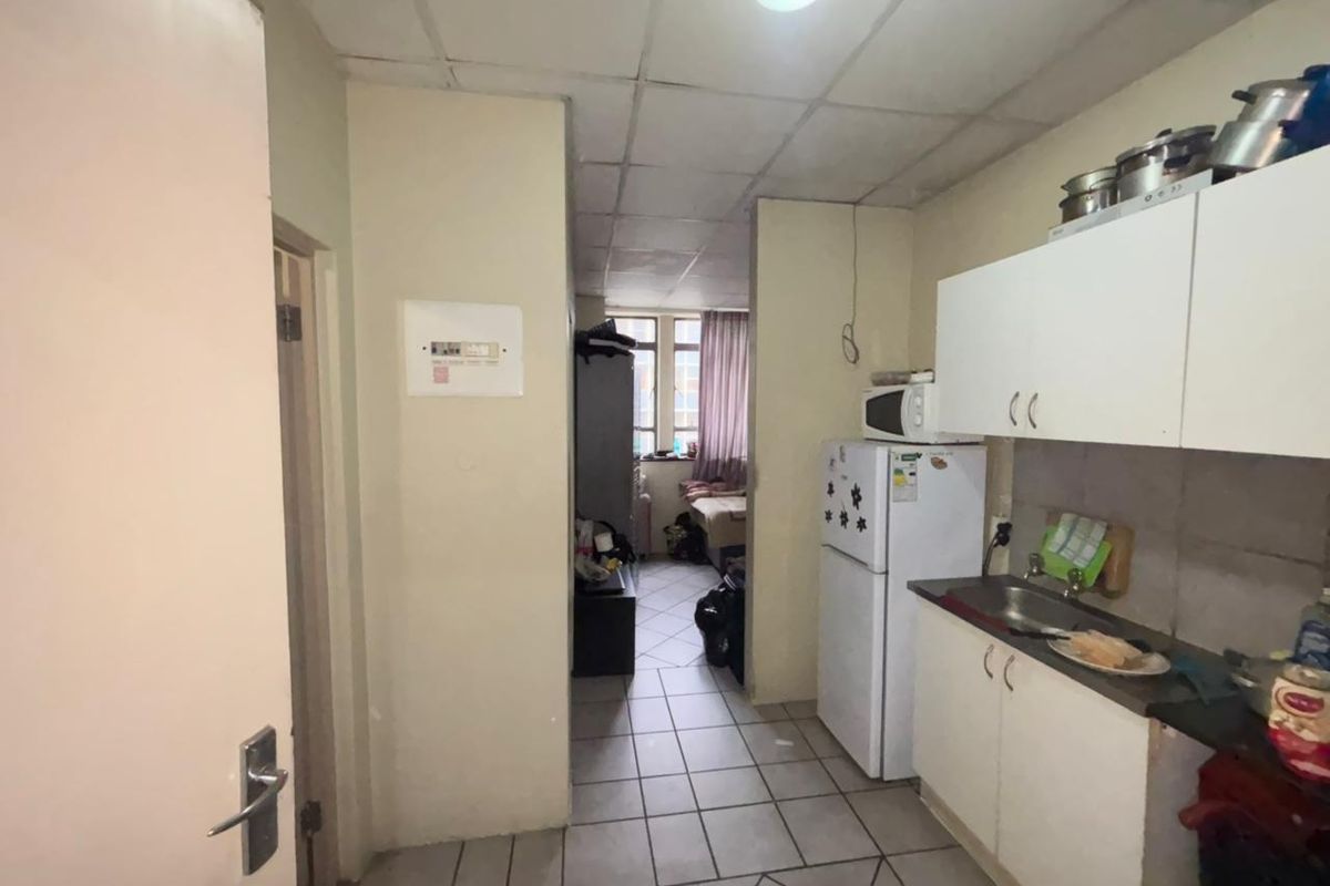 A compact kitchen area featuring built-in cabinetry, a stainless steel sink, and tiled flooring, requiring cosmetic updates to improve its overall condition.