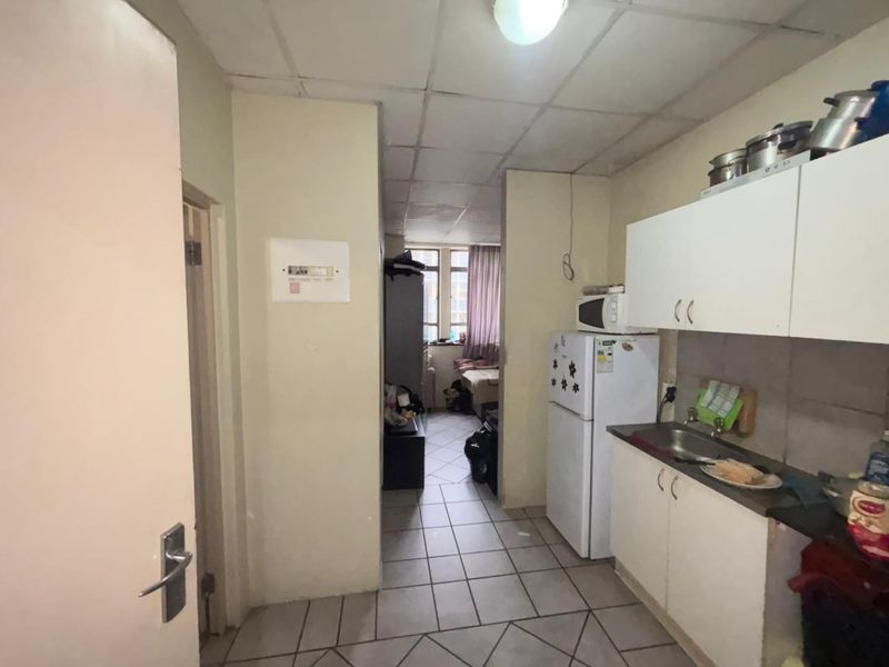 A compact kitchen area featuring built-in cabinetry, a stainless steel sink, and tiled flooring, requiring cosmetic updates to improve its overall condition.