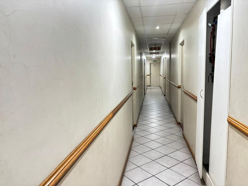 A long, empty apartment hallway featuring tiled flooring, chair rail molding, and a drop ceiling with recessed lighting.