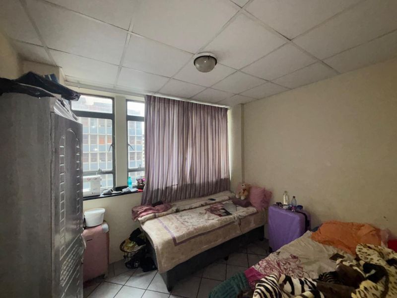 A bedroom featuring tiled flooring and a drop ceiling, with large windows providing natural light. The space requires cosmetic updates to improve its overall condition.