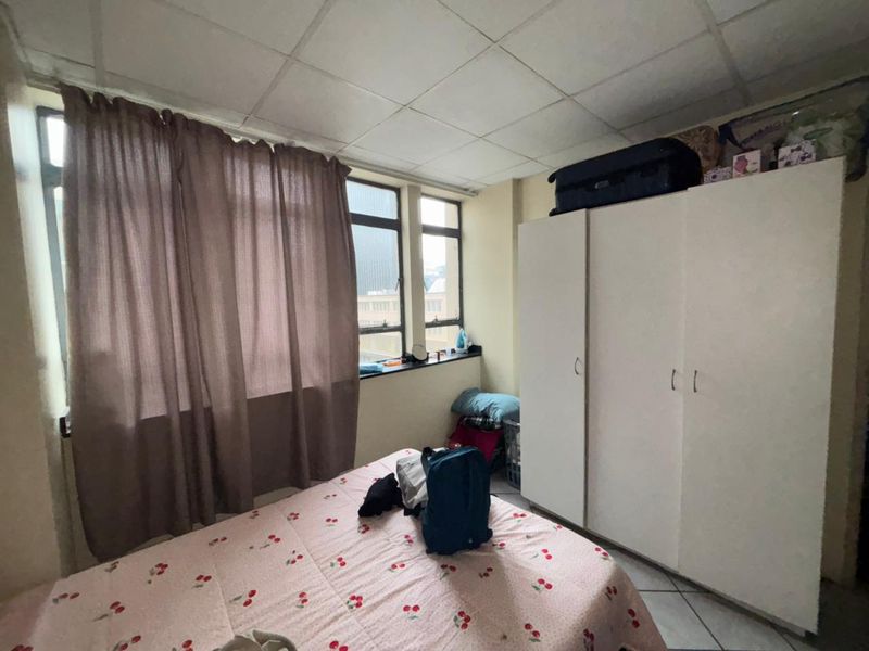 A bedroom featuring a built-in wardrobe, tiled flooring, and a drop ceiling, offering a functional space with potential for cosmetic updates.