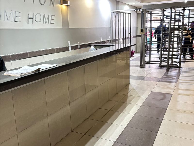 A building reception area featuring a tiled service counter, security turnstile access, and recessed ceiling lighting.