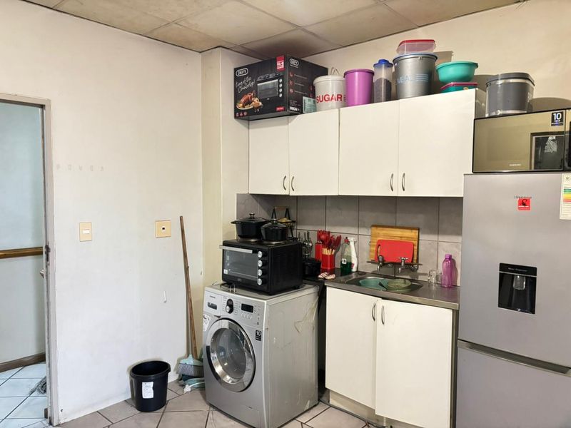 A compact kitchen area featuring white built-in cabinetry, a stainless steel sink, and tiled backsplash, requiring cosmetic updates to improve its overall condition.