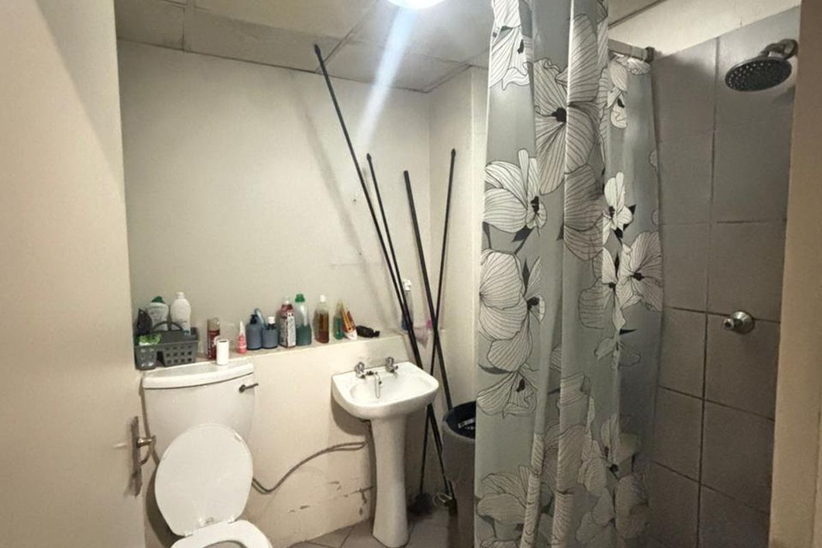 A compact bathroom featuring a pedestal basin, toilet, and a tiled shower enclosure with a drop ceiling, currently requiring maintenance and cosmetic updates.