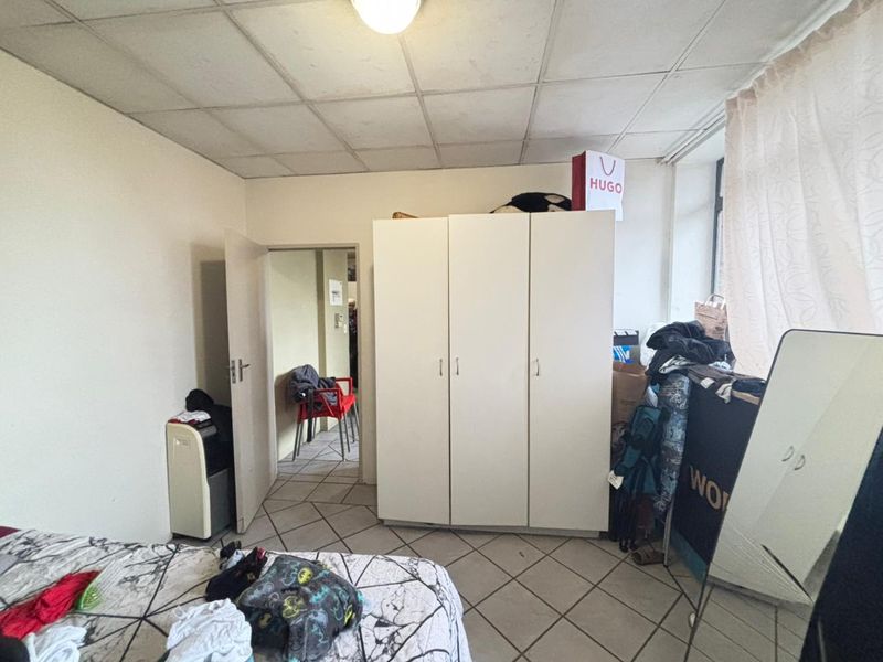 A bedroom featuring tiled flooring and a drop ceiling, currently used for storage with visible wear on the ceiling panels.