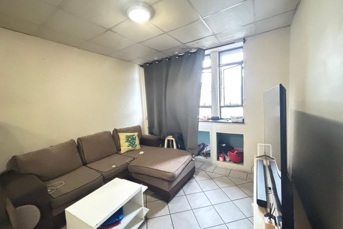 A living room featuring tiled flooring, a drop ceiling, and built-in wall niches beneath a window.