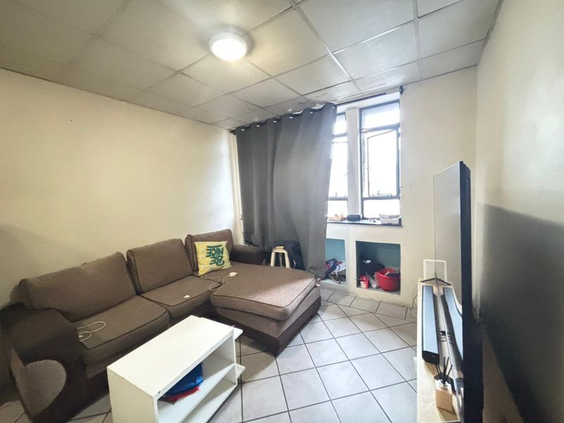 A living room featuring tiled flooring, a drop ceiling, and built-in wall niches beneath a window.