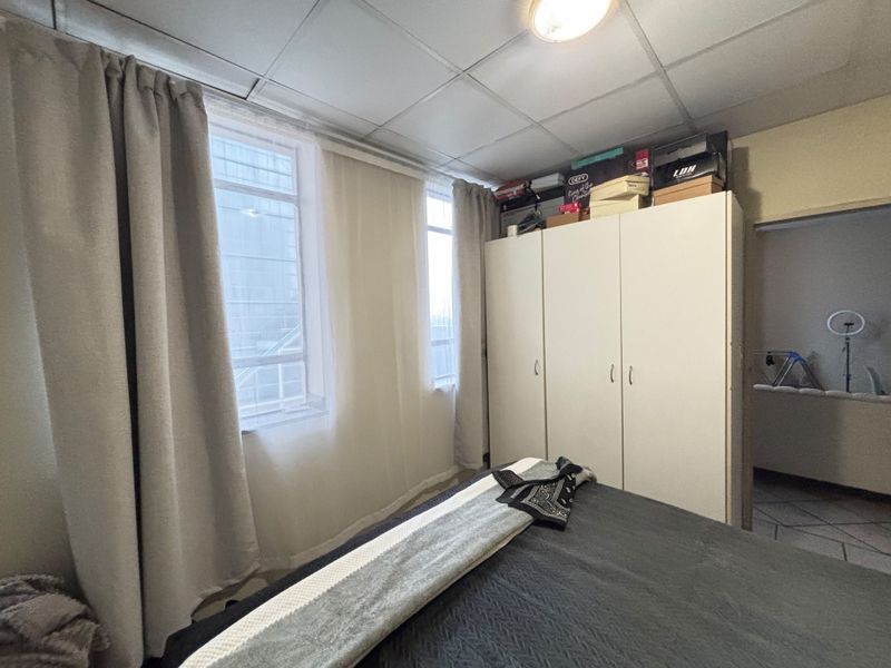 A bedroom featuring a built-in wardrobe and drop ceiling tiles, offering a functional space with natural light from the windows.