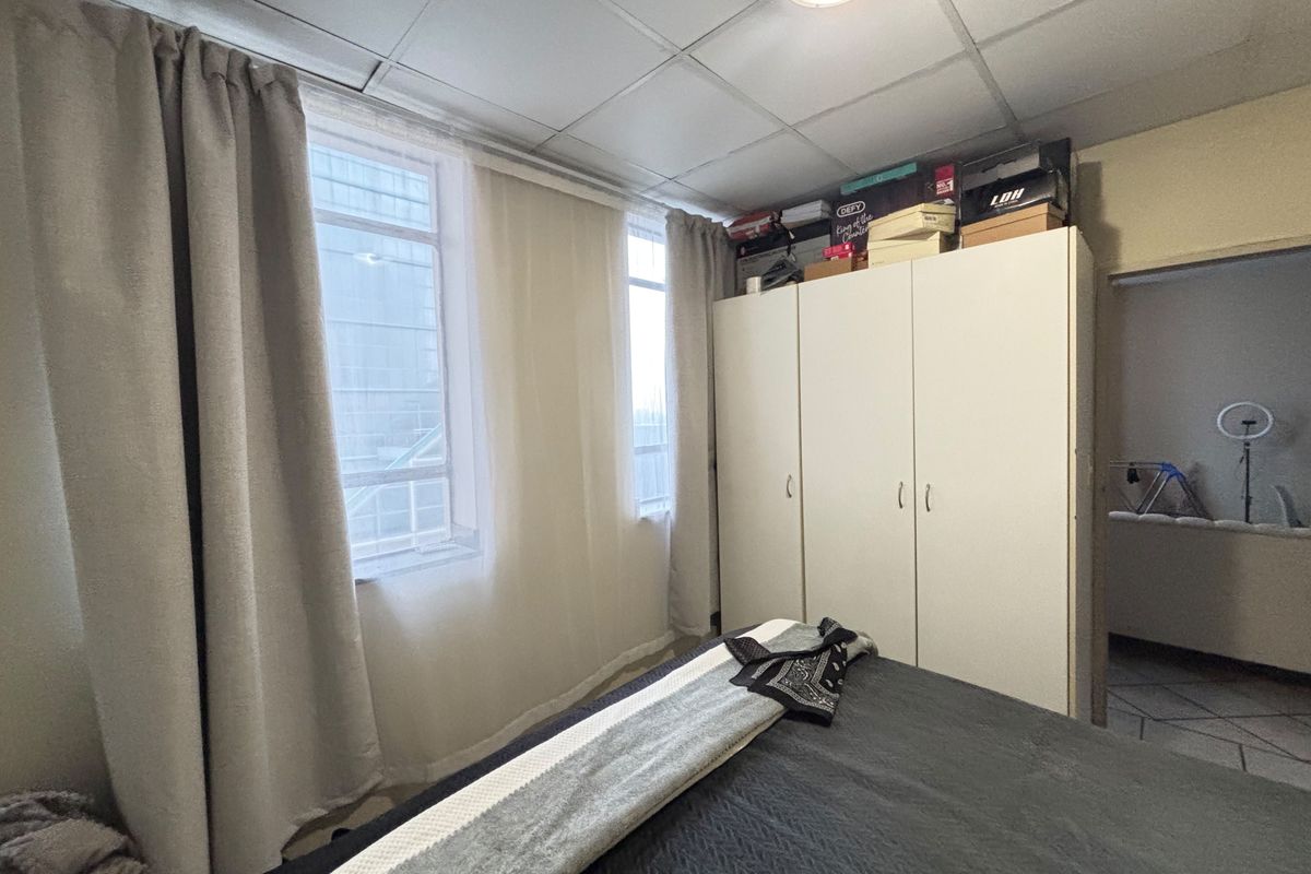 A bedroom featuring a built-in wardrobe and drop ceiling tiles, offering a functional space with natural light from the windows.