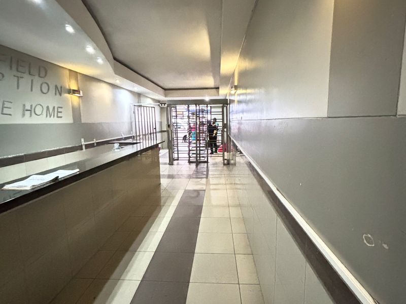 A functional apartment building entrance lobby featuring a reception desk, tiled flooring, and a secure turnstile access point.