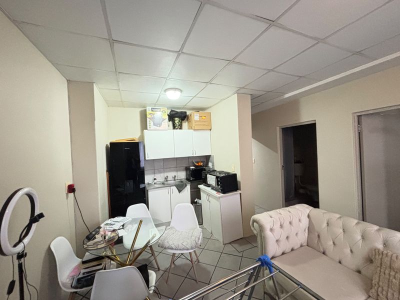 Open plan living and kitchen area featuring a drop ceiling, tiled flooring, and basic kitchen cabinetry with a stainless steel sink.