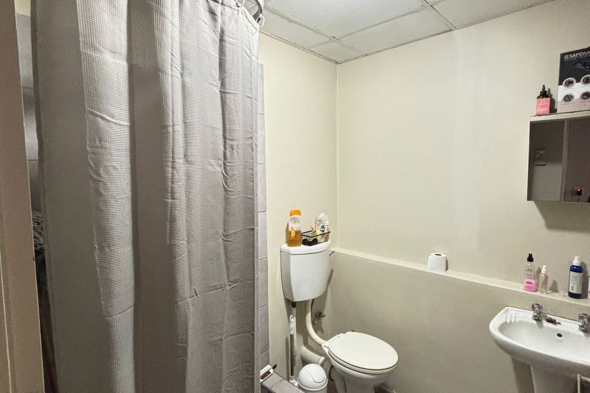 A functional bathroom featuring a pedestal basin, toilet, and shower area with a curtain, requiring cosmetic updates to improve its dated appearance.