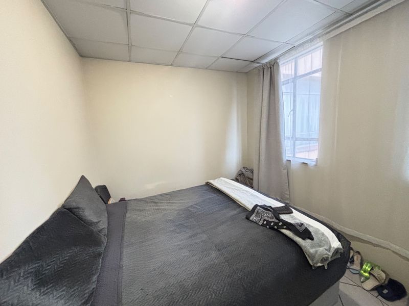 A bedroom featuring a drop ceiling, tiled flooring, and a window. The room shows signs of wear and requires cosmetic updates.