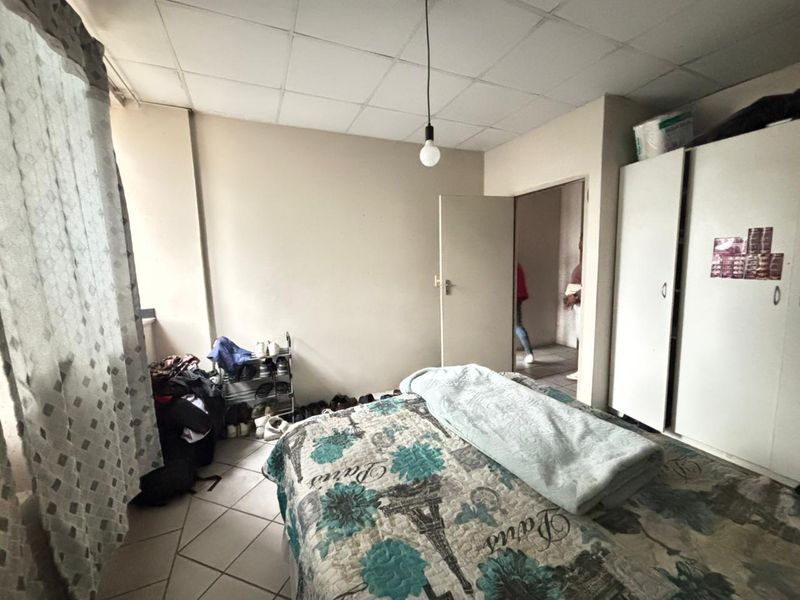 A bedroom featuring tiled flooring, a built-in wardrobe, and a drop ceiling, requiring cosmetic updates to improve its overall condition.