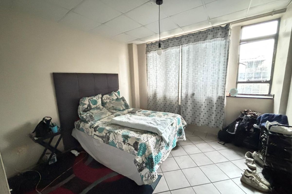 A bedroom featuring tiled flooring and a drop ceiling, offering a functional space with natural light from a large window.