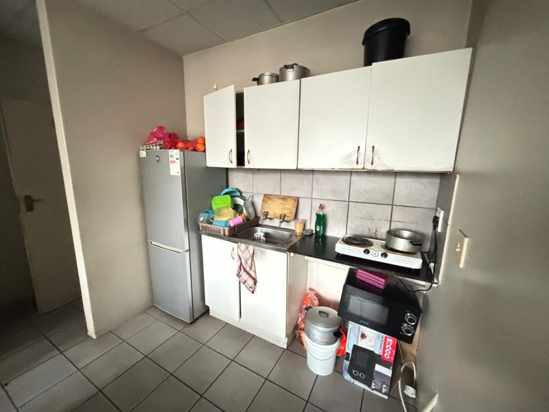 Compact kitchen area featuring basic built-in cabinetry, a stainless steel sink, and tiled flooring, requiring cosmetic updates to improve functionality and aesthetic appeal.