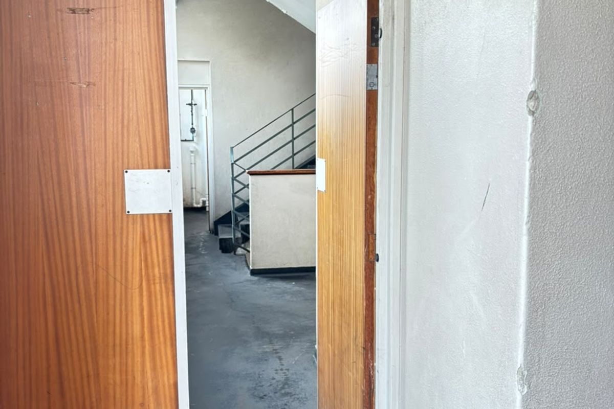 A functional apartment building hallway featuring wooden fire doors, an emergency exit sign, and access to a communal staircase.