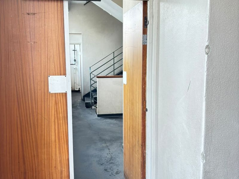 A functional apartment building hallway featuring wooden fire doors, an emergency exit sign, and access to a communal staircase.