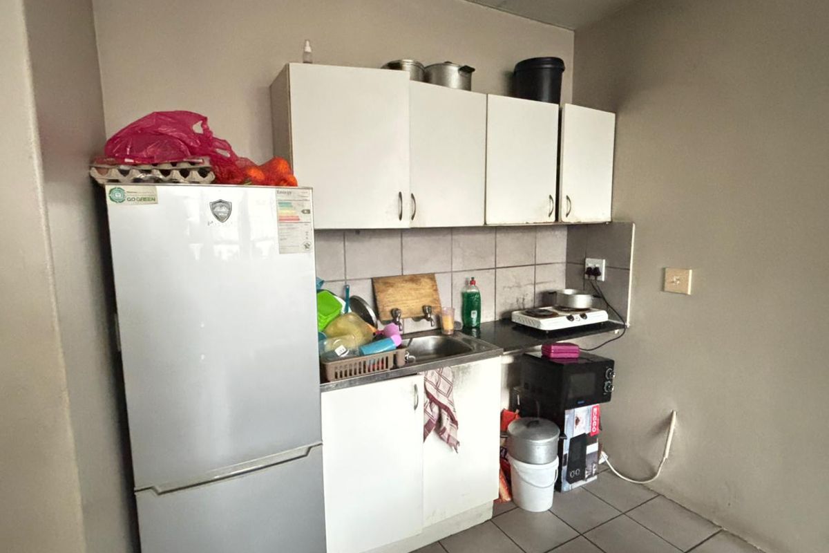 A compact kitchen area featuring basic cabinetry, a stainless steel sink, tiled backsplash, and tiled flooring, suitable for a small apartment layout.