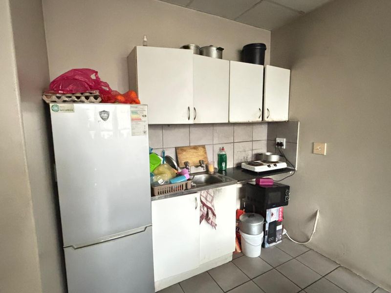 A compact kitchen area featuring basic cabinetry, a stainless steel sink, tiled backsplash, and tiled flooring, suitable for a small apartment layout.