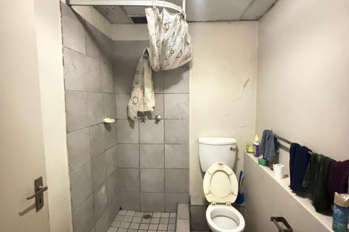 A compact bathroom featuring a tiled shower cubicle, toilet, and washbasin, requiring significant cosmetic updates and ceiling repairs.