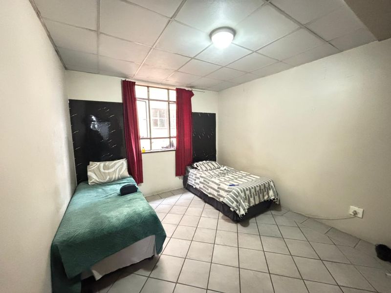 A bedroom featuring tiled flooring and a drop ceiling, with a metal frame window providing natural light.