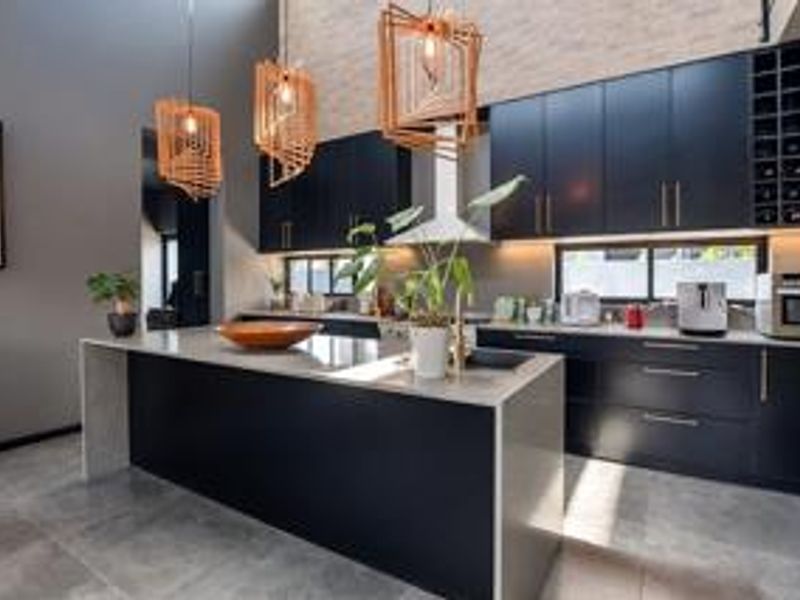 Modern kitchen featuring dark cabinetry, a large stone-topped island, integrated wine storage, and high-quality finishes with a double-volume ceiling.