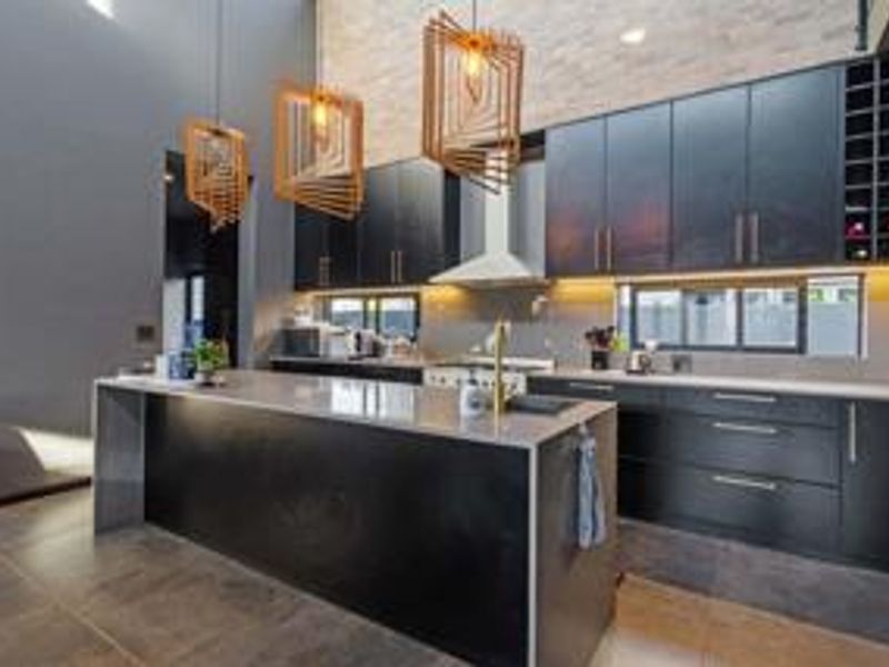 Modern kitchen featuring sleek black cabinetry, a large central island with stone countertops, integrated wine storage, and high-end finishes throughout.